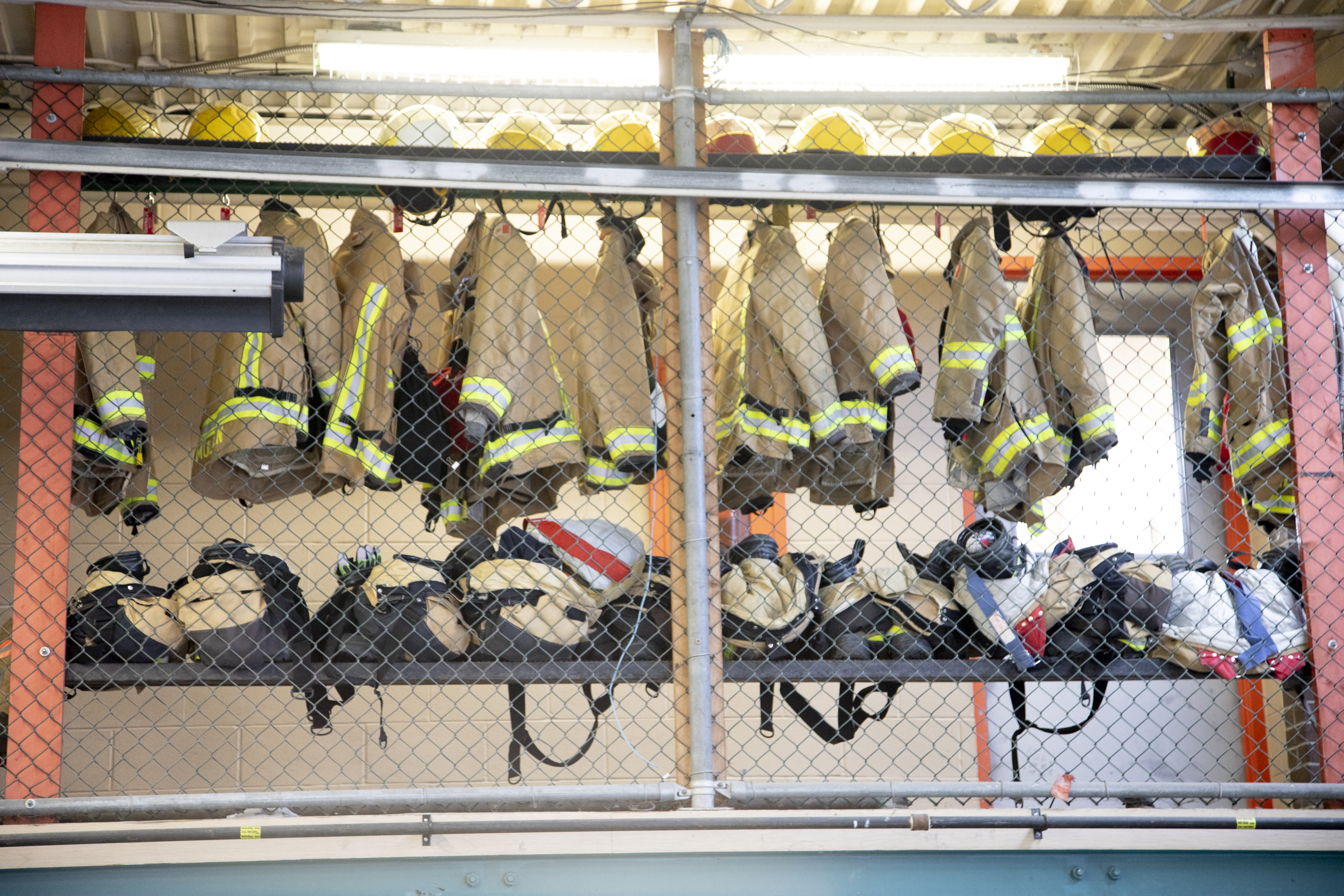 Firefighter gear including coats and helmets hanging in caged locker