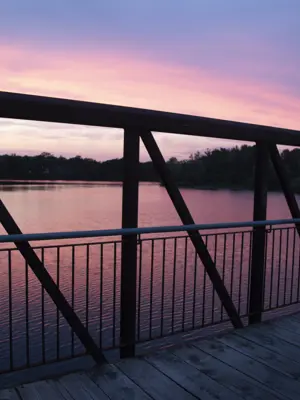Railing of footbridge overlooking river at sunset