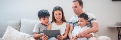 Woman, man, and two children sitting together on a couch looking at a tablet