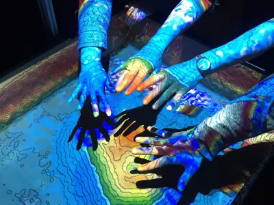 Arms and hands extending over a table with a blue and yellow light projecting onto the arms and hands