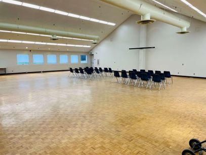 A look inside the Naval Park's Admiralty Hall. A wooden floor with several rows of chairs, white walls, high ceilings, and much space for standing