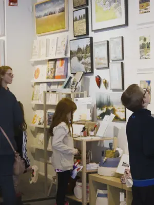 Families in the Art Gallery of Peterborough's gallery shop looking at different items on the walls.