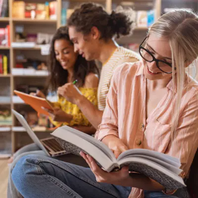 Three students sitting on the floor of a library reading books