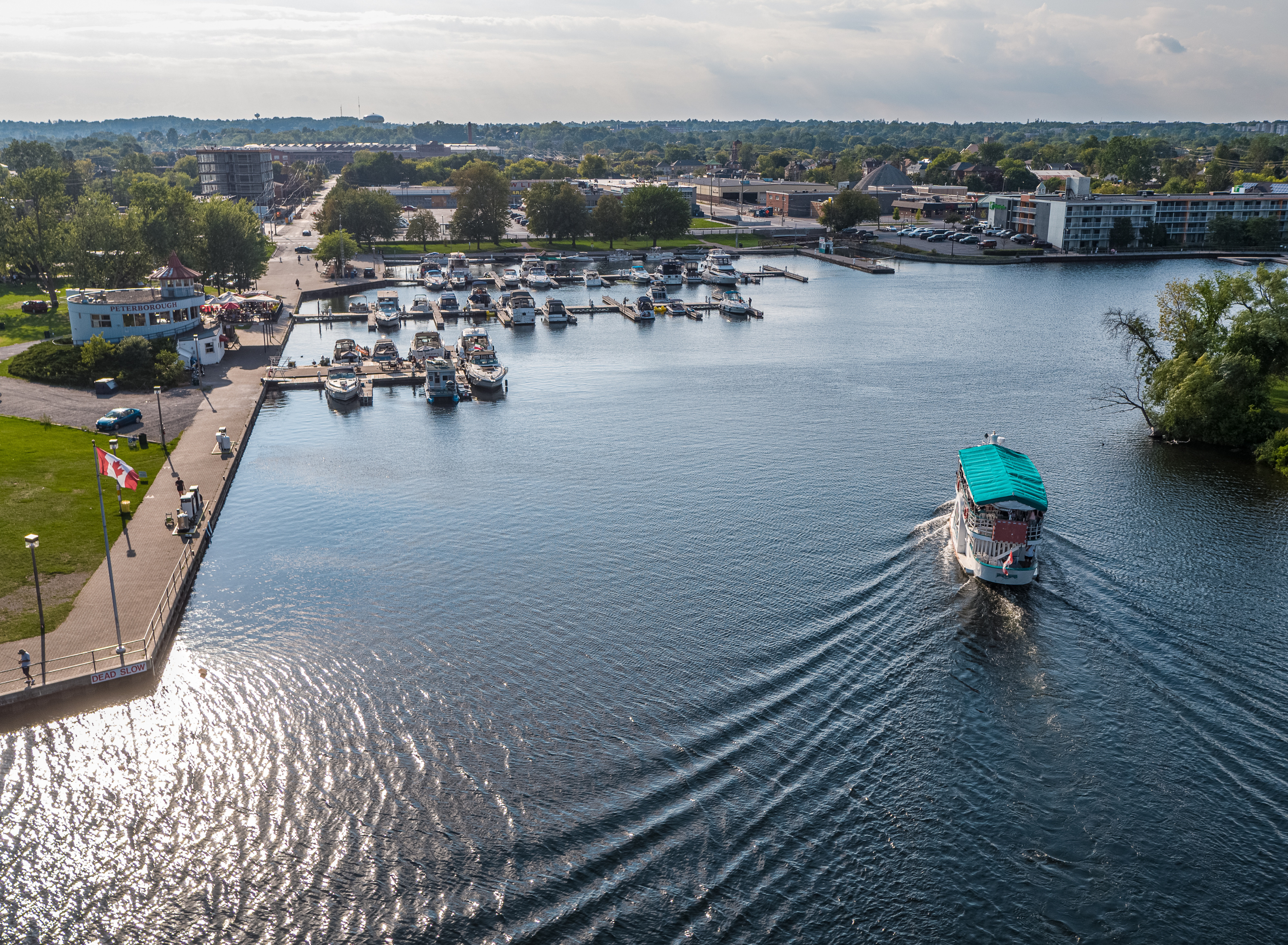  Sightseeing cruise boat approaches marina coming off of Little Lake in Peterborough. Marina, Holiday Inn hotel and Del Crary Park are in the background.