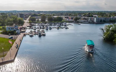 Sightseeing cruise boat approaches marina coming off of Little Lake in Peterborough. Marina, Holiday Inn hotel and Del Crary Park are in the background.