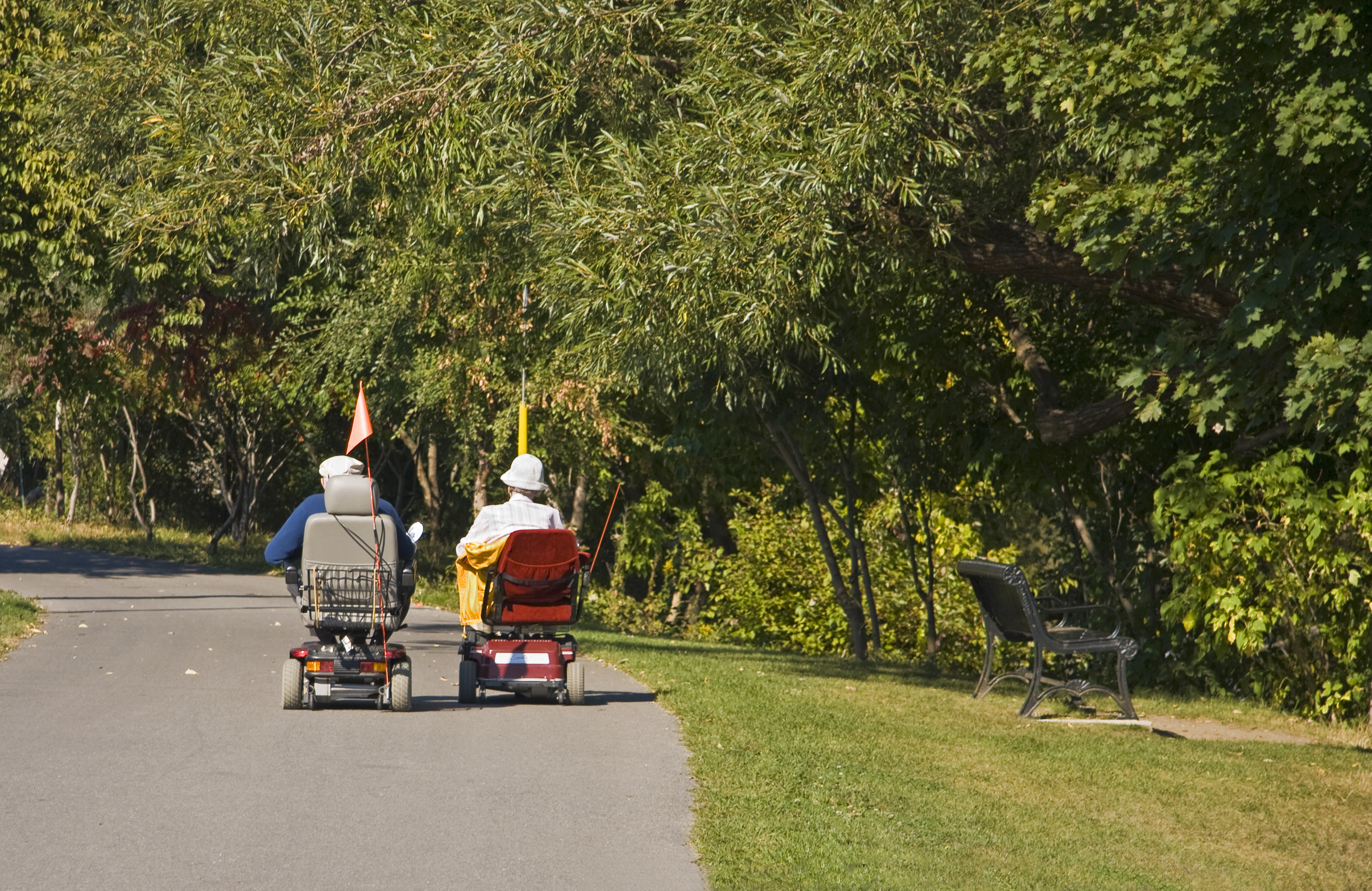 Two people on electric scooter mobility devices on a park trail