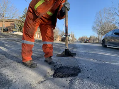 A pot hole is filled with asphalt and tamped down in the winter