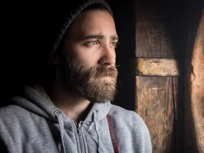 Man with a beard, wearing a beanie, looking out a window