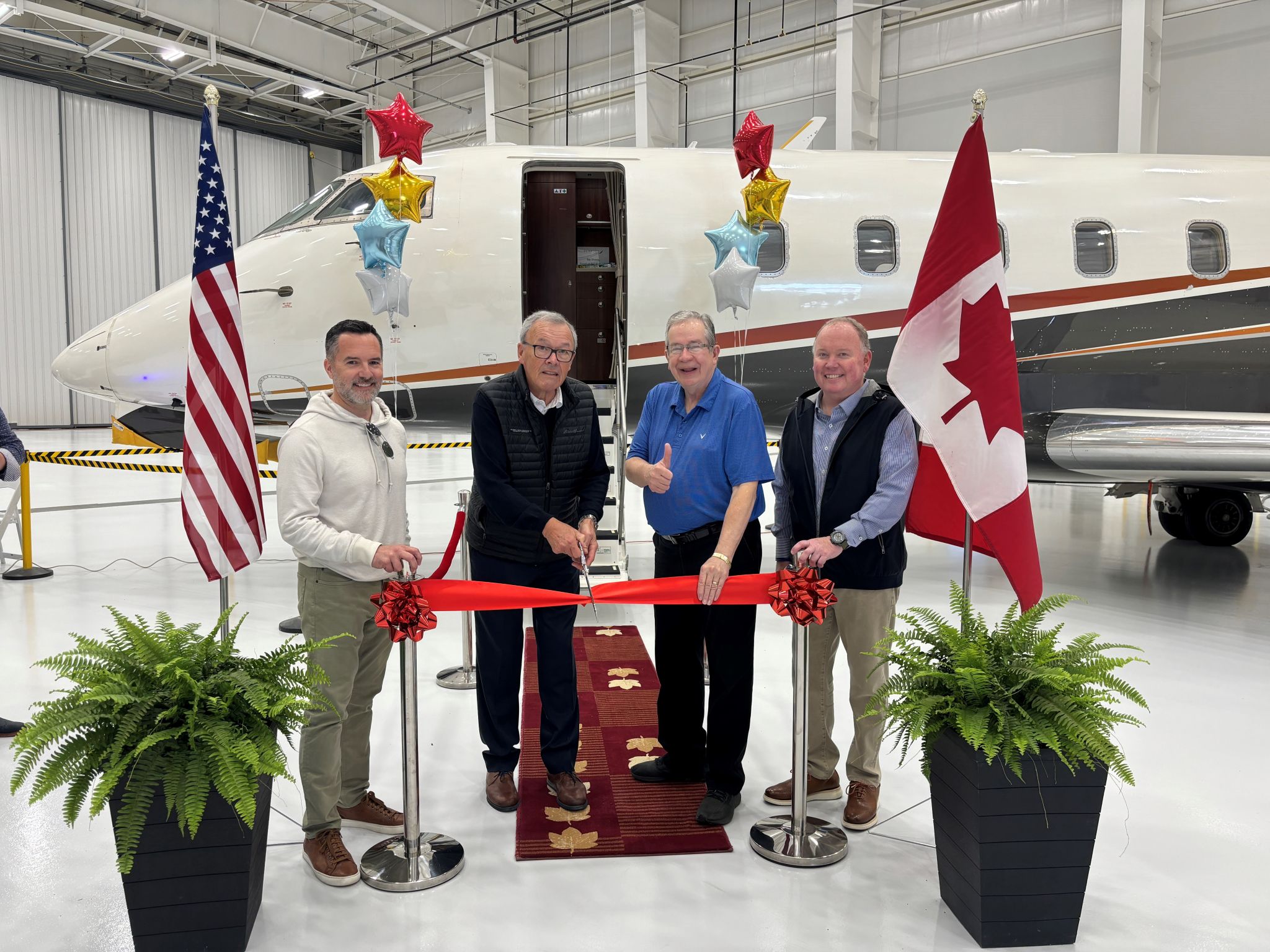 Four people standing behind a ribbon for a ribbon cutting ceremony next to a plane