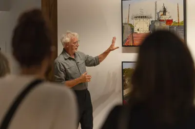 Artist gesturing toward painting on wall with people watching